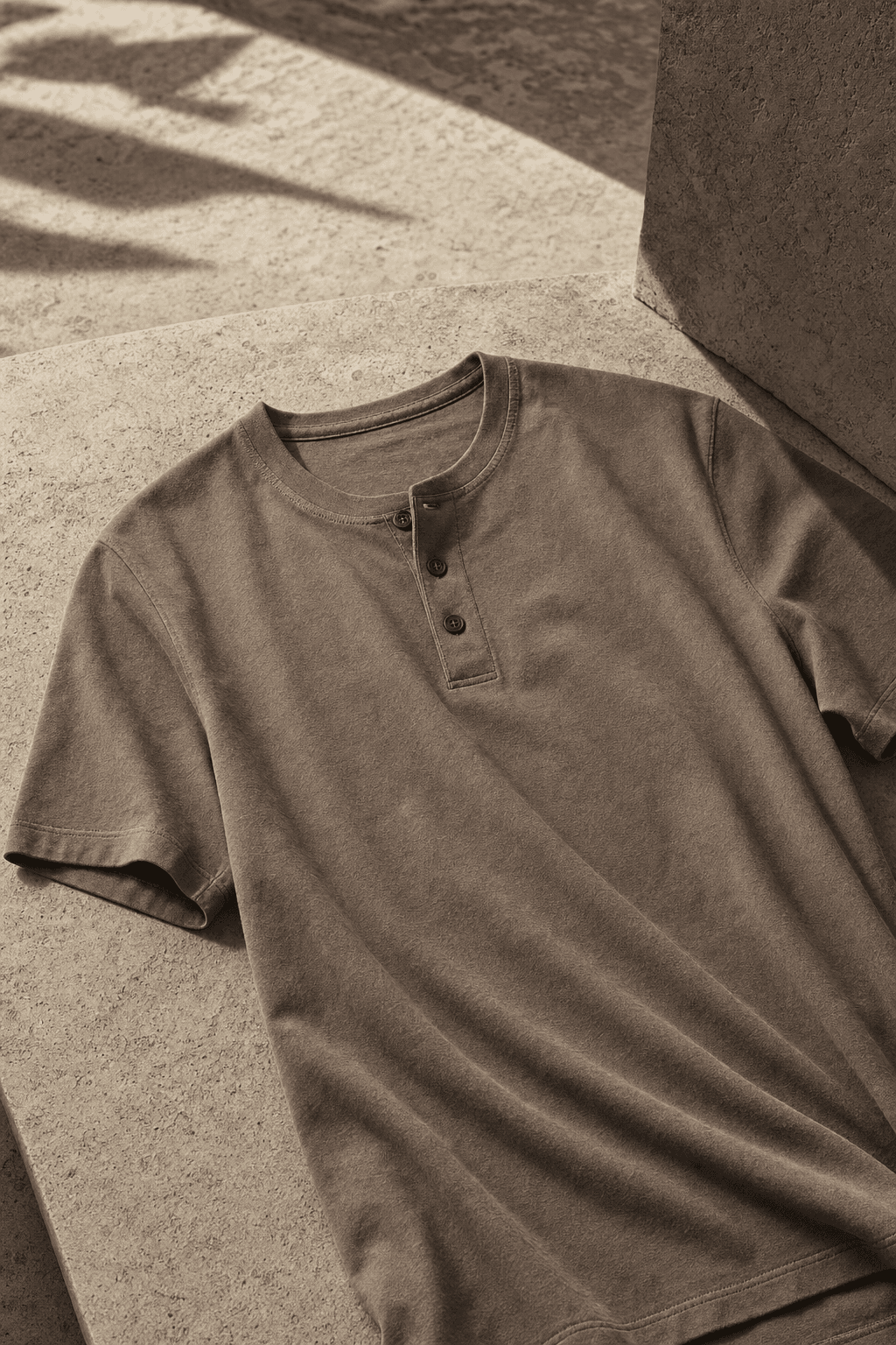 Taupe Henley shirt laid on warm stone with its collar and button placket visible